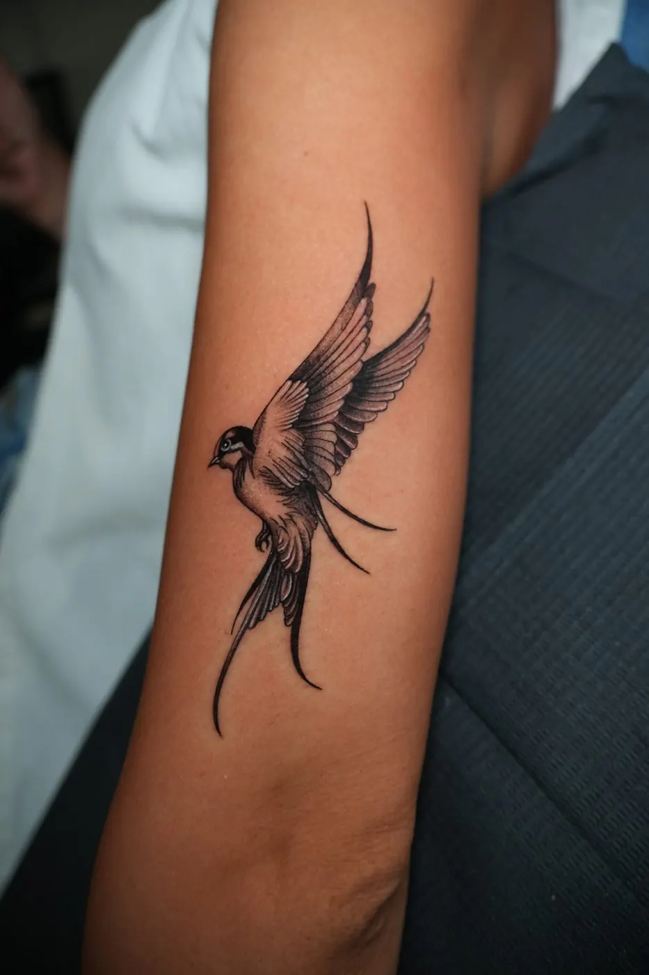 Black and grey swallow in flight tattooed on a forearm