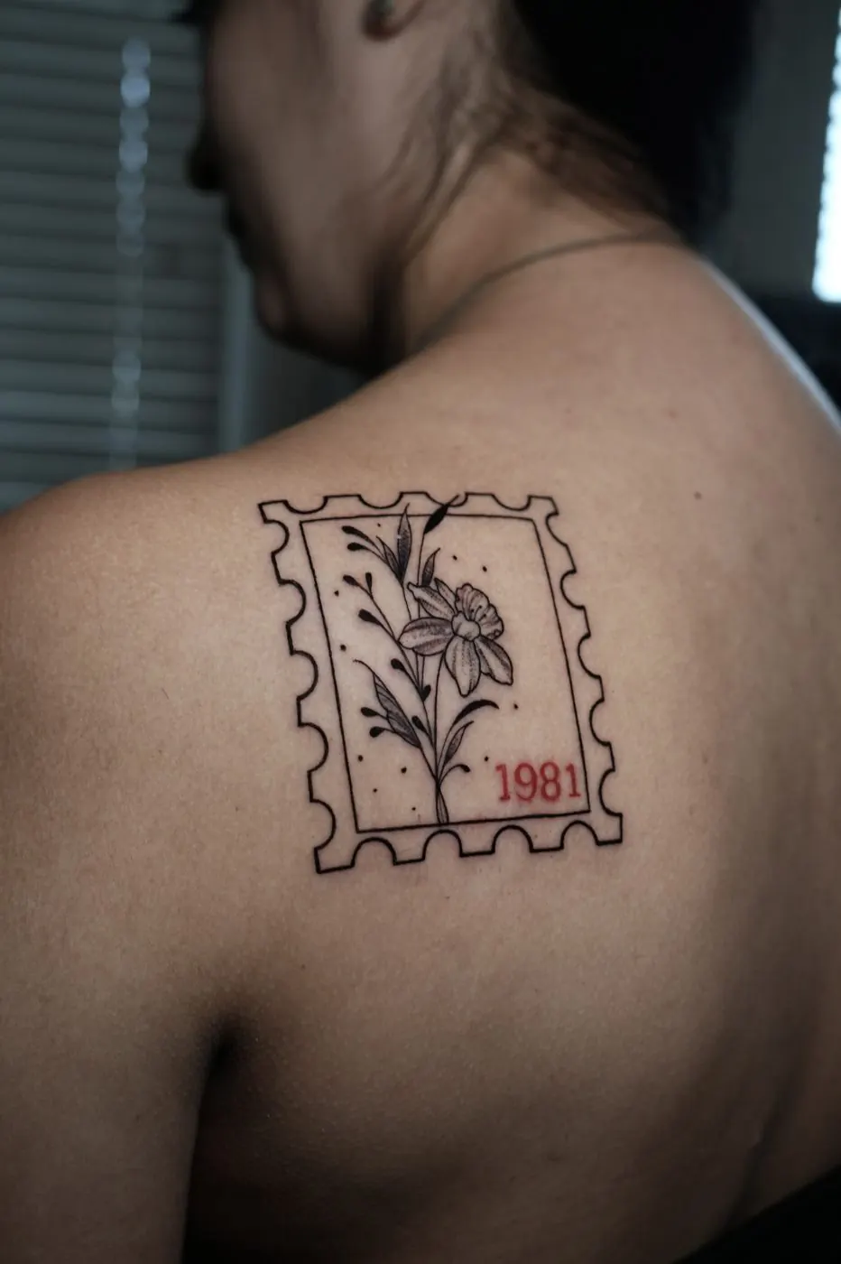 Framed flower stamp tattoo on a shoulder