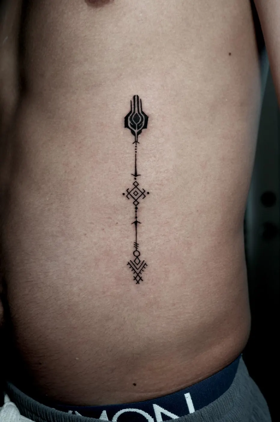 Fine line ornamental dagger tattoo running down the ribs