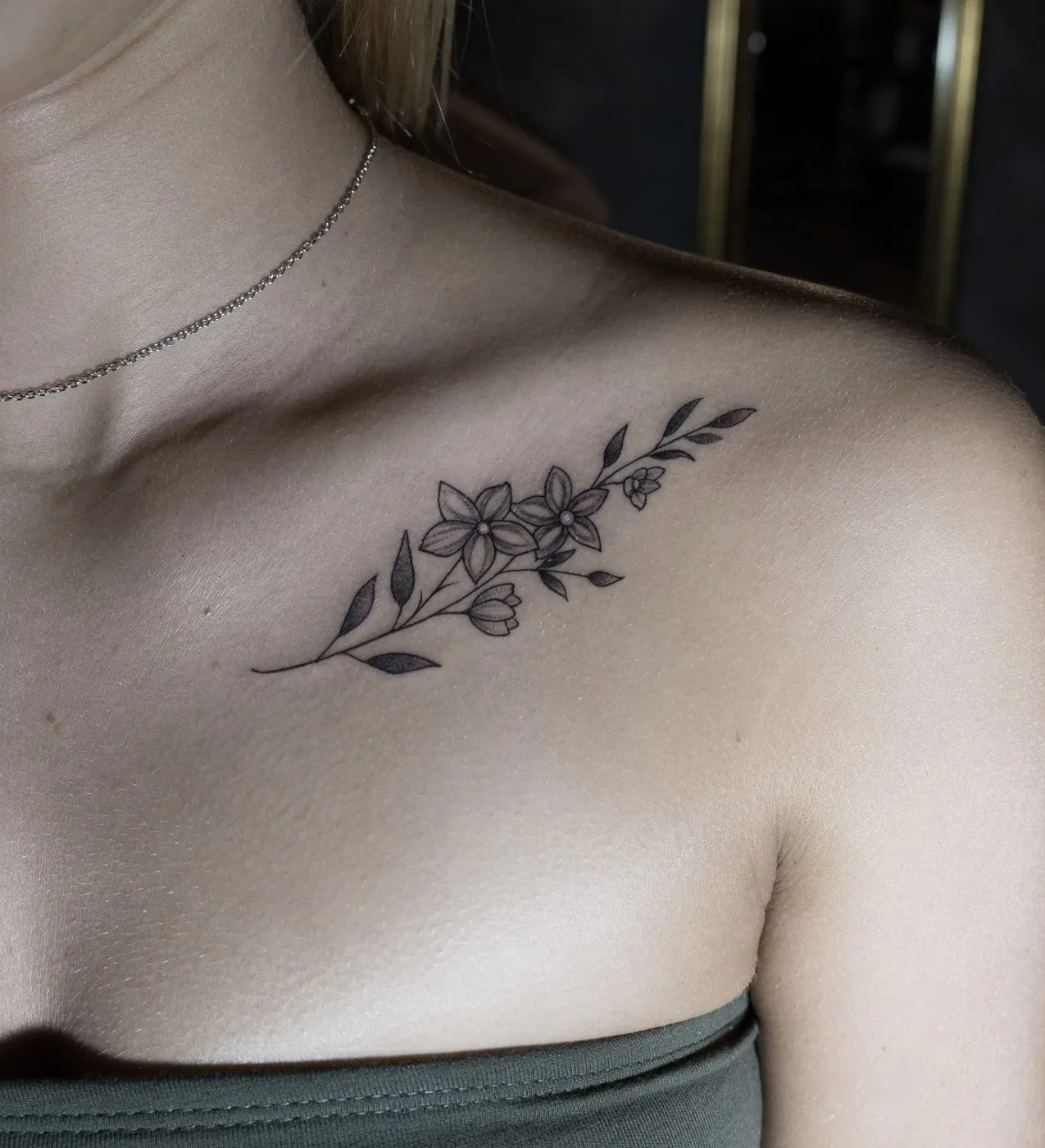 Fine line floral branch tattoo on the collarbone